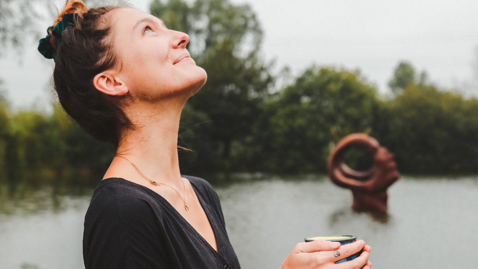 Sweet & Wild Treats founder, Teddie, holding a warming turmeric latte by a lake looking up into the sky